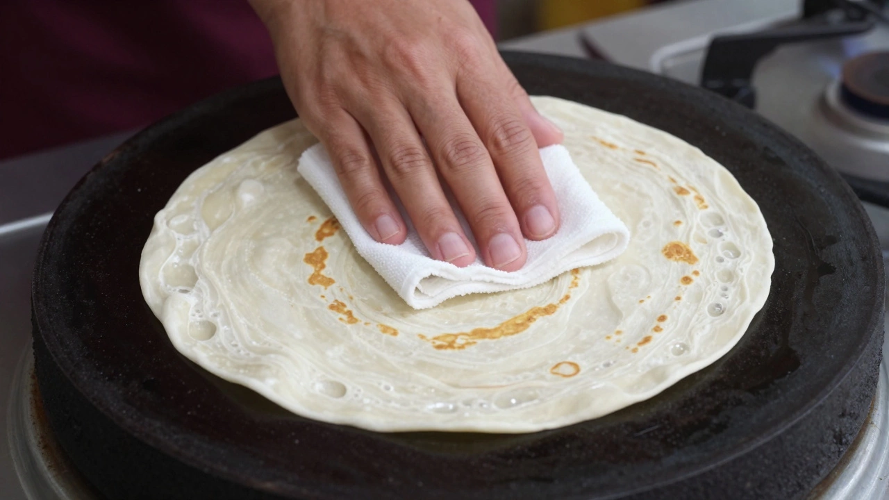 Raw roti puffing up on a hot cast-iron tawa while being pressed with a cloth