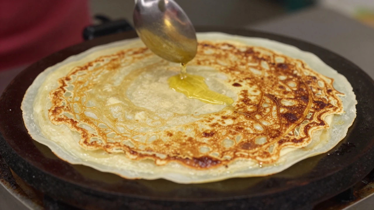 Close-up of a crispy dosa frying on a hot griddle with oil being drizzled.